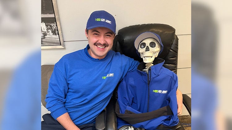 1-800-GOT-JUNK? team member smiling next to a skeleton decoration wearing a 1-800-GOT-JUNK? jacket 1-800-GOT-JUNK? team member smiling next to a skeleton decoration wearing a 1-800-GOT-JUNK? jacket