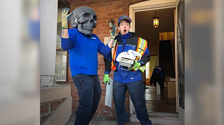 One 1-800-GOT-JUNK? team member looking shocked while the other team member wears a skull mask One 1-800-GOT-JUNK? team member looking shocked while the other team member wears a skull mask