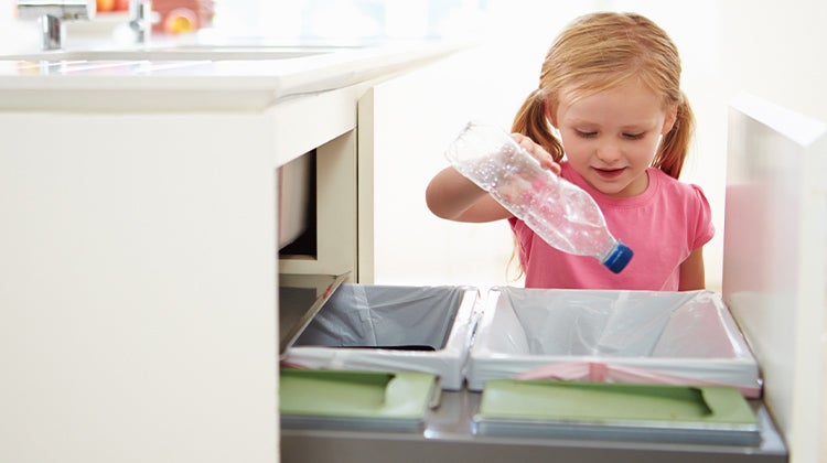 Young girl putting an empty bottle into the recycling under the sink Young girl putting an empty bottle into the recycling under the sink
