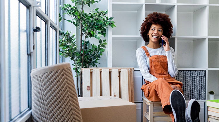 Woman smiling on the phone with moving boxes around her Woman smiling on the phone with moving boxes around her